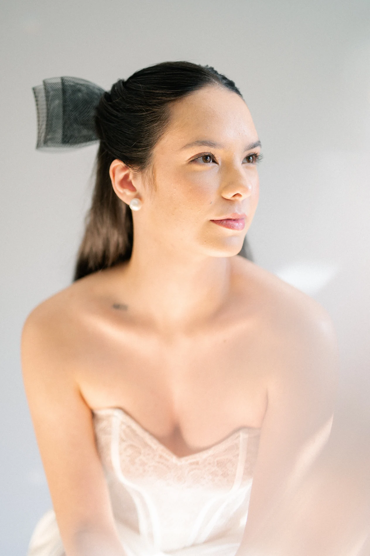 Bridal portrait with soft makeup and an updo finished with a black bow.