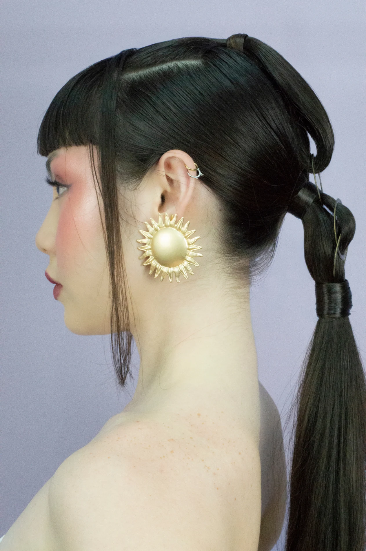 Profile of a graphic hairstyle with aligned strands and a gold earring.